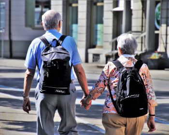 Älteres Paar läuft Hand in Hand und mit Rucksack durch eine Stadt